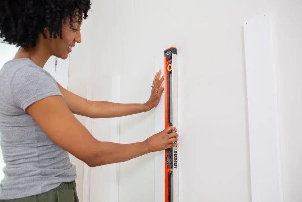 The next step in this DIY accent wall project is to install vertical trim boards, using a level to ensure they are plumb.
